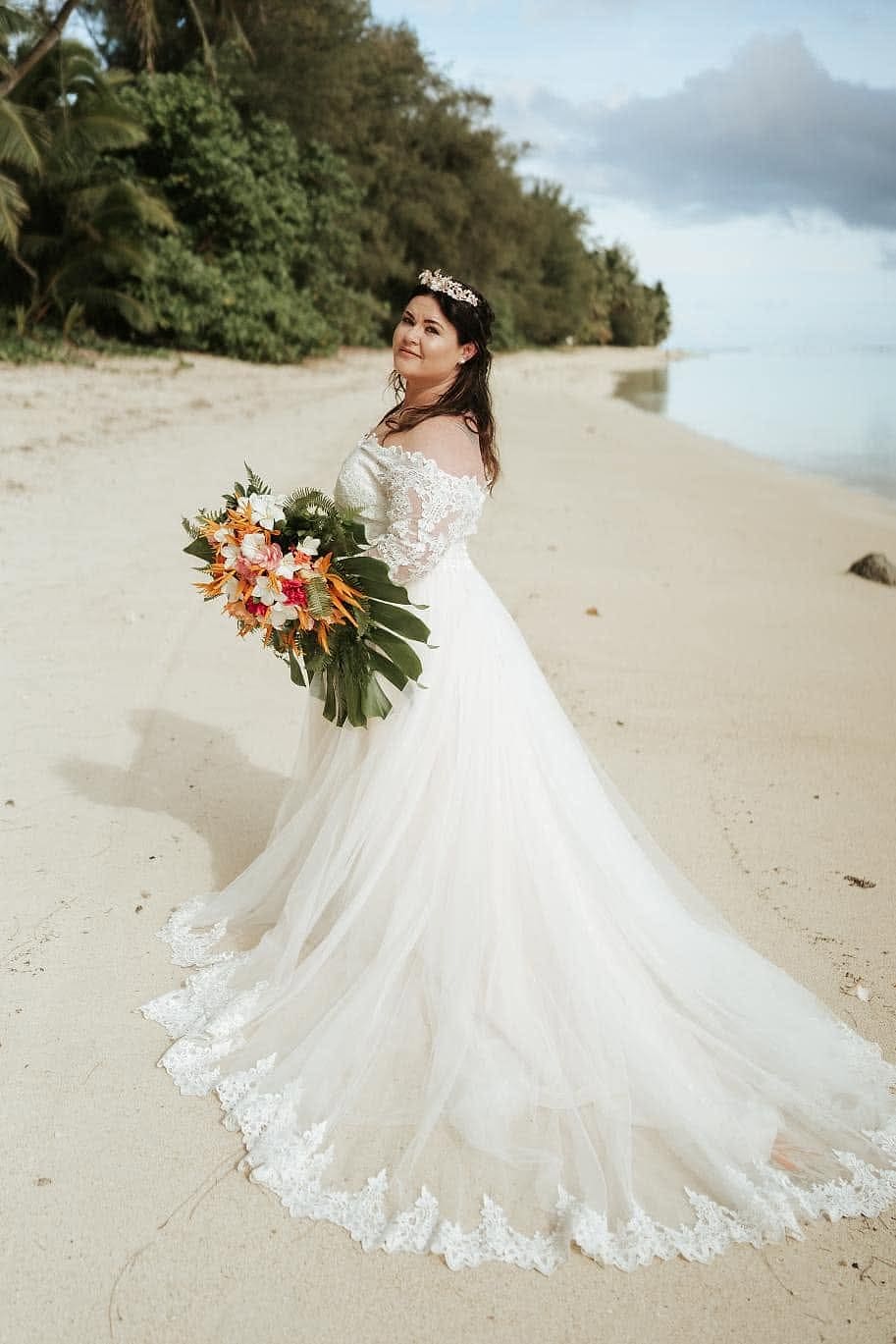 Bride on a beach in an off-the-shoulder lace gown with a tulle skirt and lace-edged train