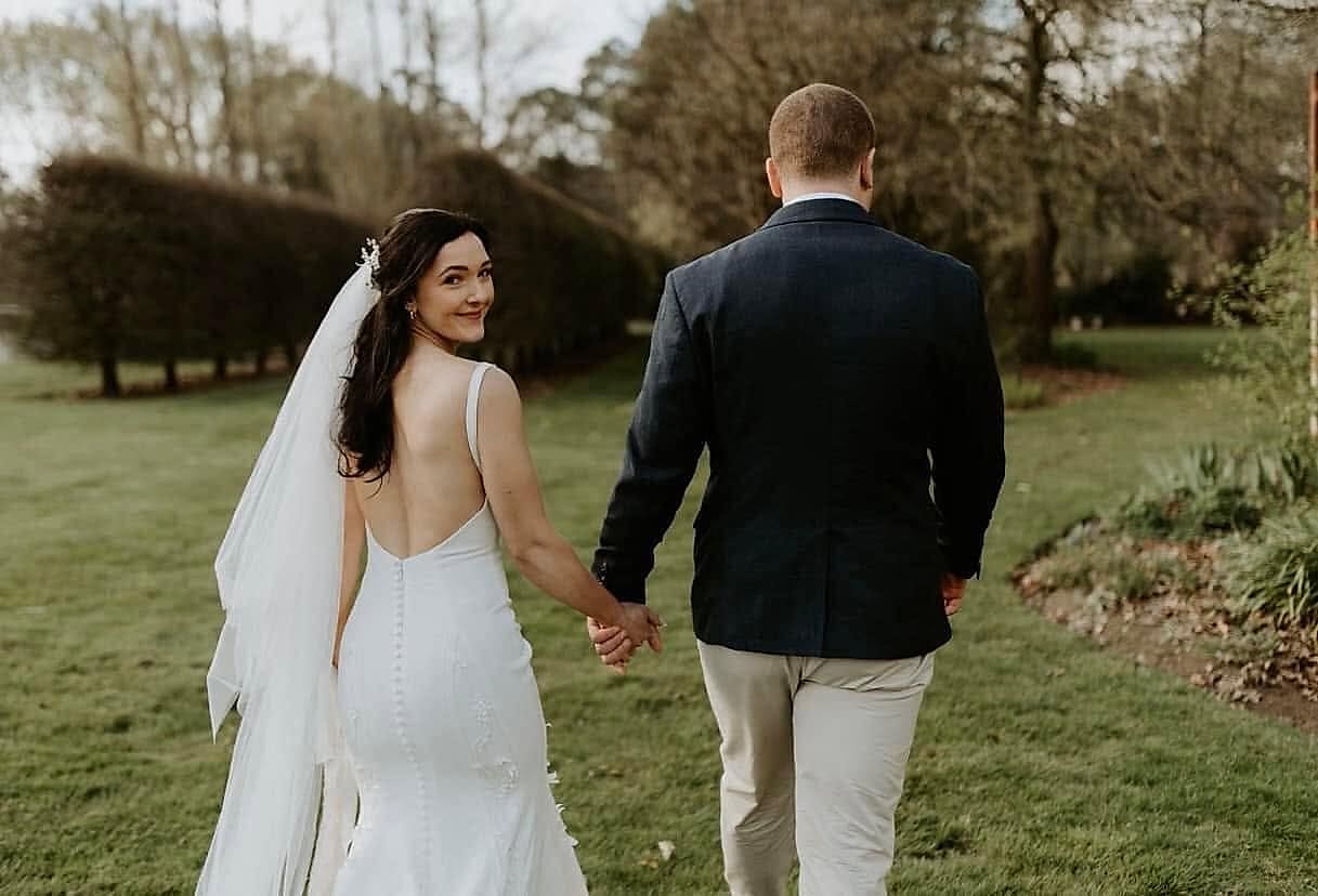 Bride looking back over her shoulder in a fitted gown with a low back and a row of covered buttons